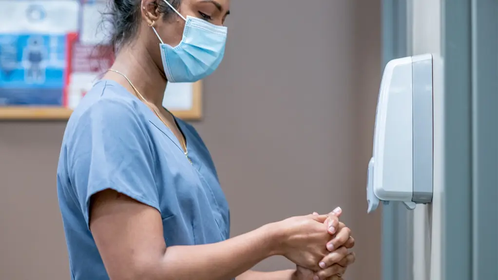 Nurse sanitizing her hands at a hand hygiene station.